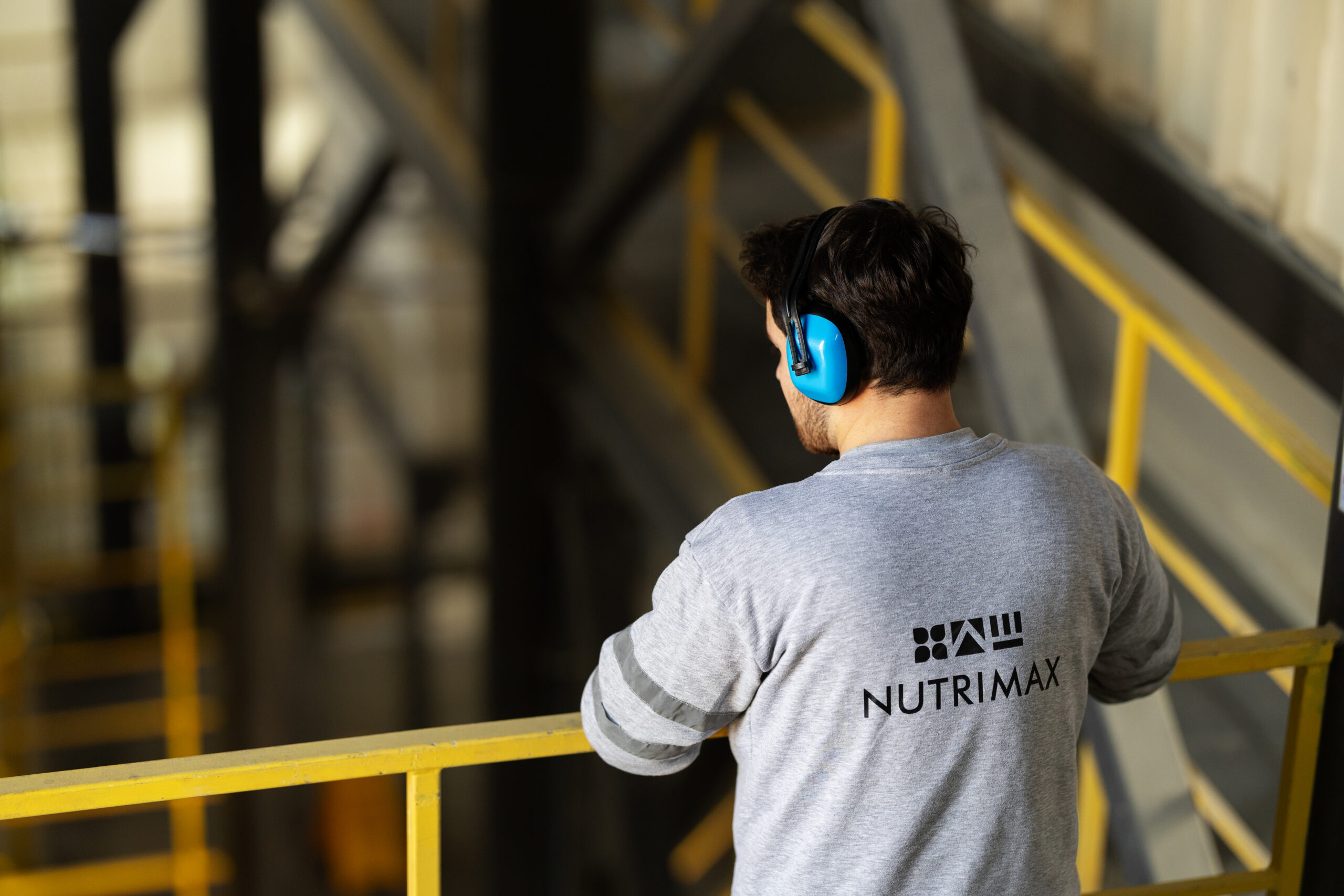 Worker in a Nutrimax shirt wearing ear protection and inspecting an industrial area