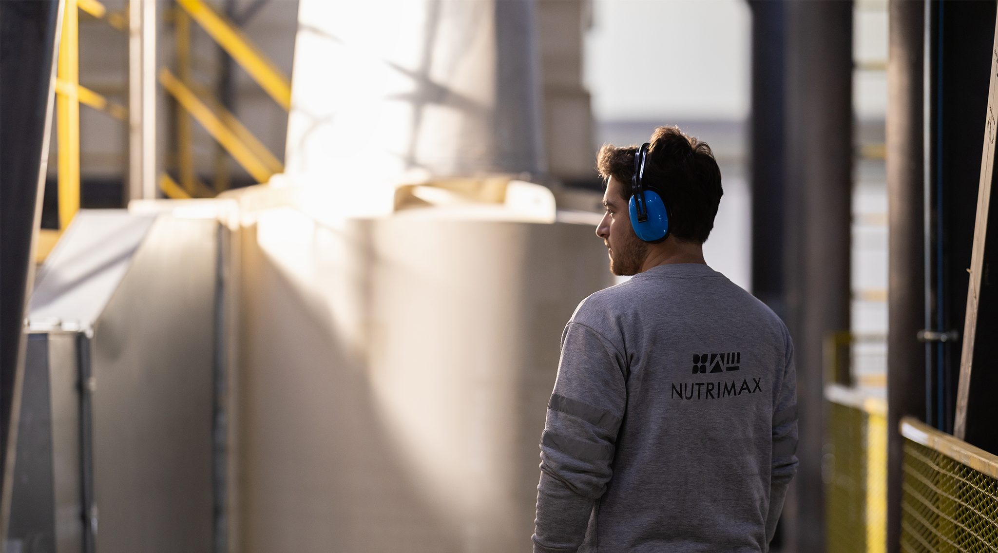 Worker in a Nutrimax shirt wearing ear protection and inspecting an industrial area